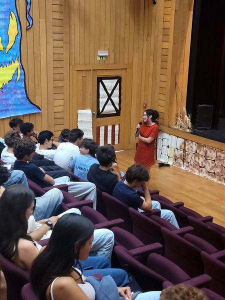 Mulher de vestido vermelho fala ao microfone com os estudantes
